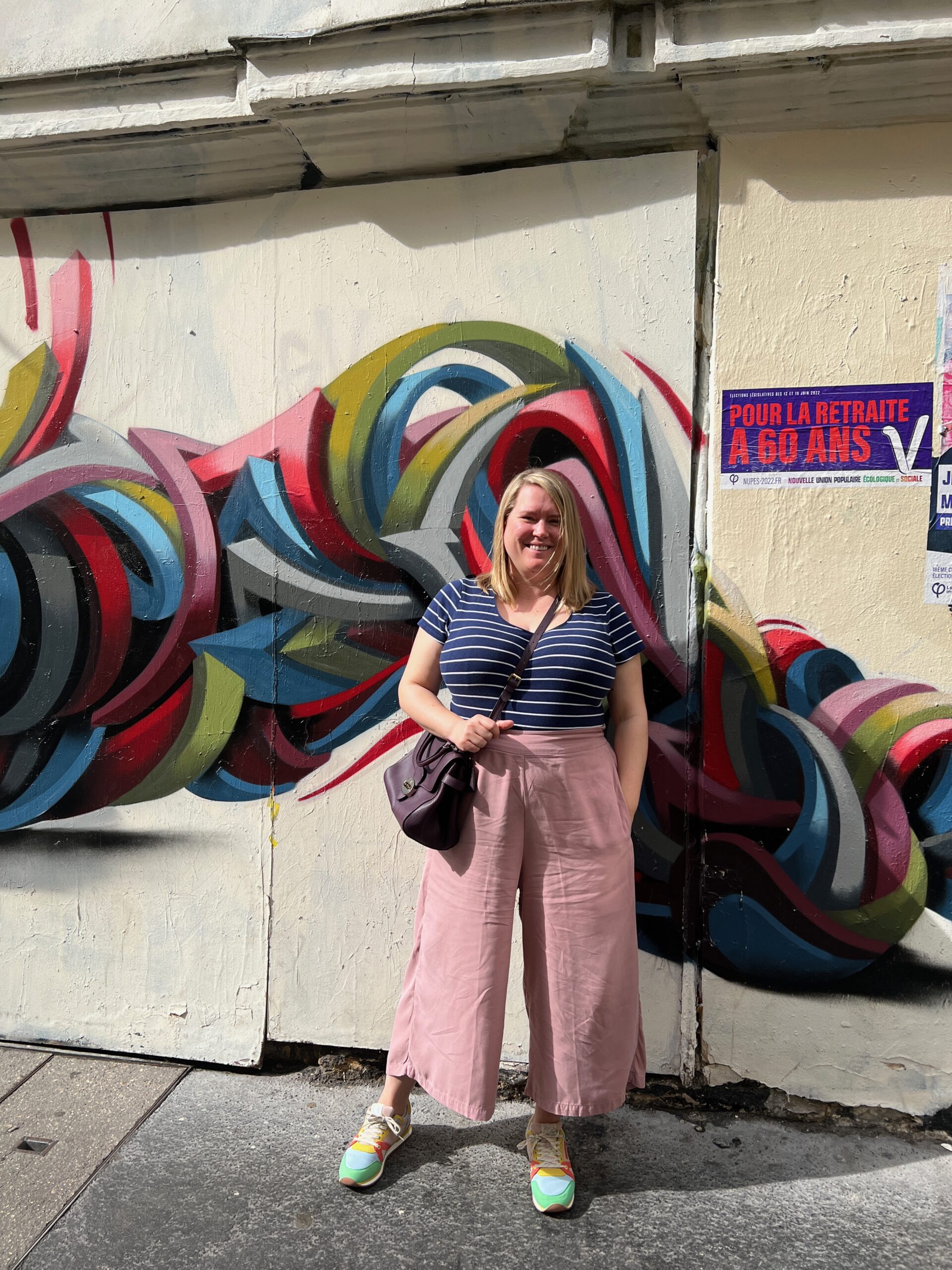 Jenny in pink trousers and a stripy top in front of a grafitti'd wall